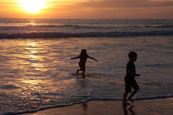 Two children play in the sea as  the sun sets.