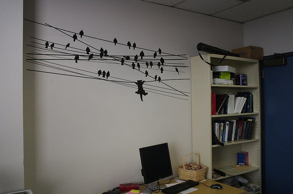 A wall decorated with birds sitting on telephone wires.