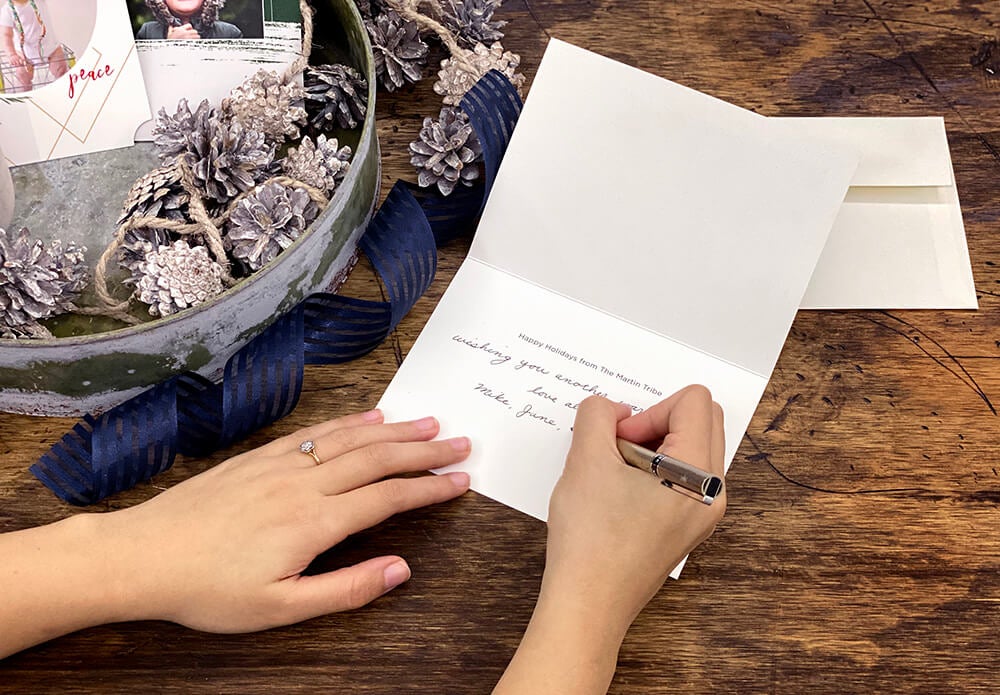 woman writing in a holiday card manufactured by printique