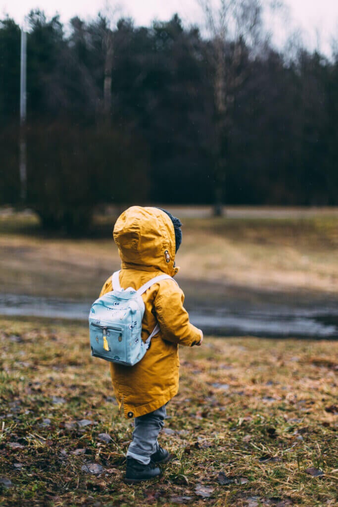 Adorable toddler in rain jacket on his way back to school.
