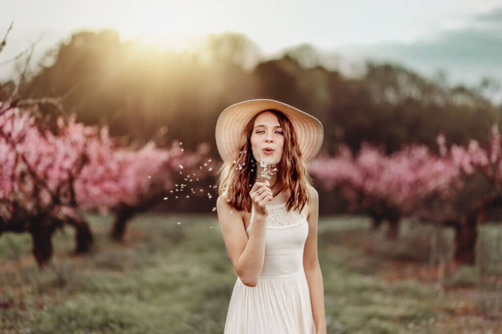 Girl blows dandelion during summer in a Georgia peach orchard.
