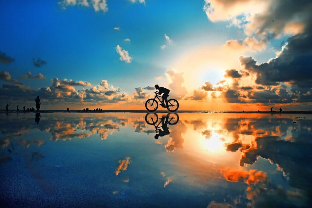 A cyclist races alongside water during a gorgeous summer sunrise.